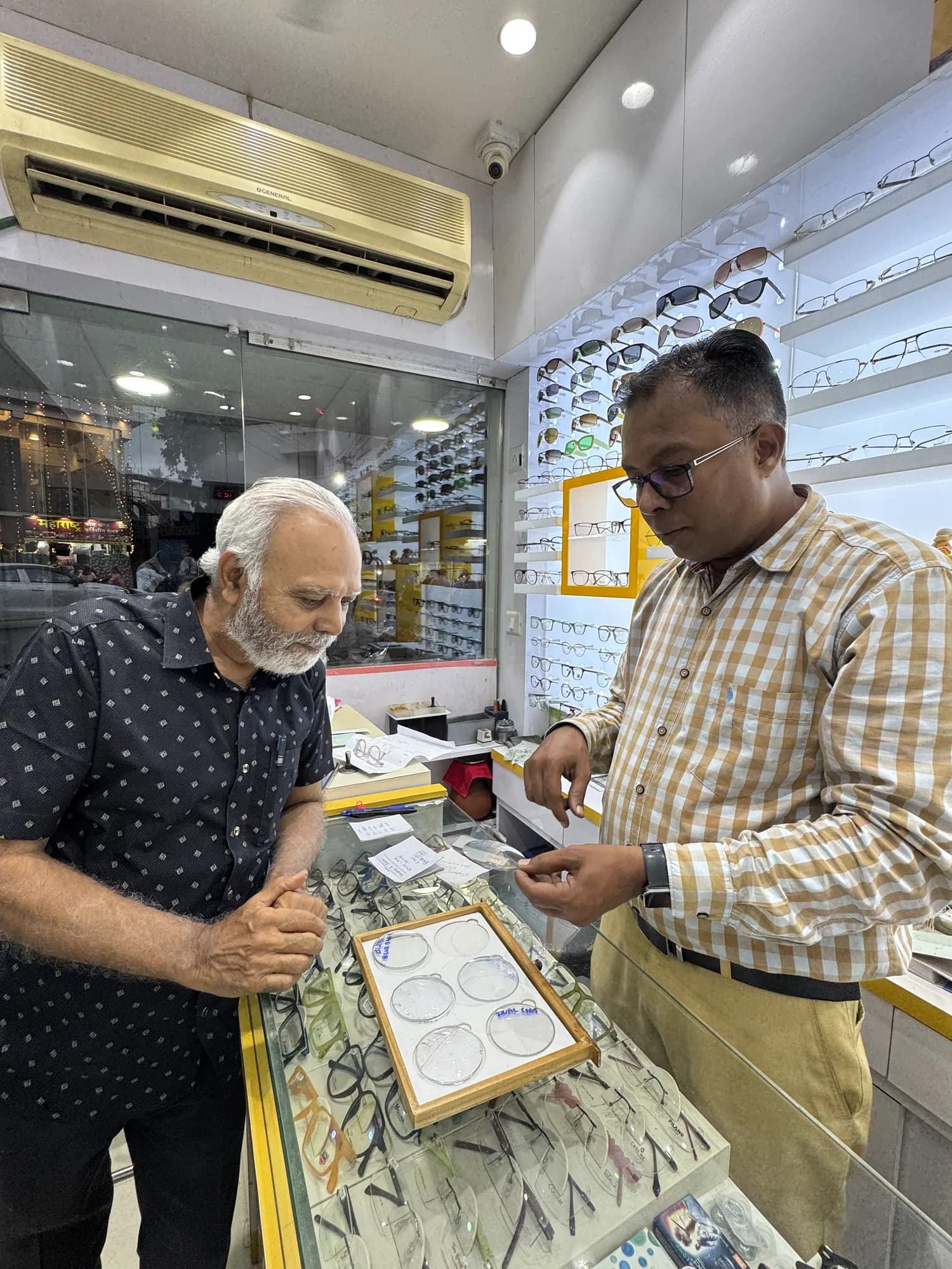 Jignesh Vora helping an elderly customer with a frame at the counter of Ami Optics, Virar East