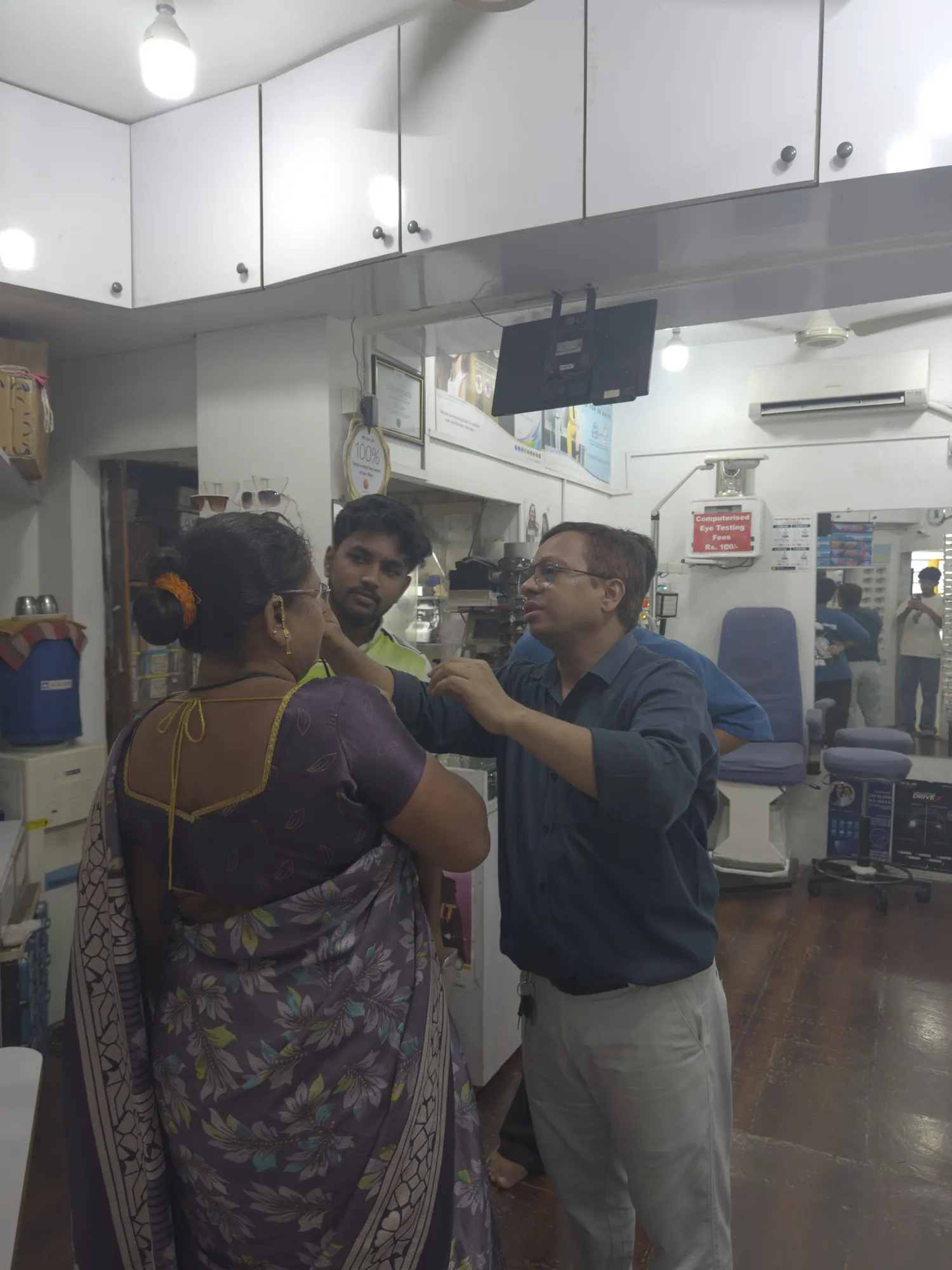A finished pair of spectacles being adjusted on a customer's face at the counter of Ami Optics