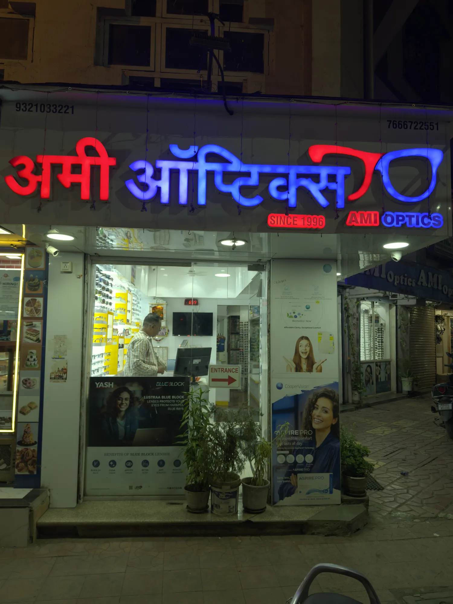 The Ami Optics shopfront on V. S. Marg, Virar East, lit up in the evening